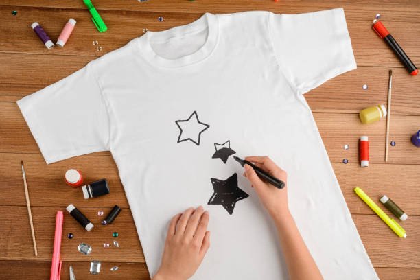 Woman drawing black stars on a white t-shirt. Handcraft talent and a little magic. Perfect custom designed gift for young daughter.